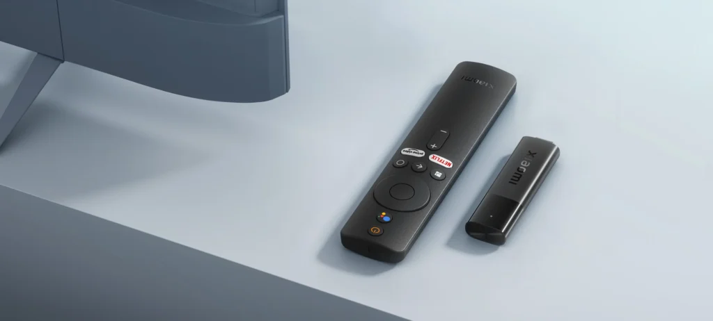 Xiaomi TV Stick y su mando a distancia con botones de acceso directo junto a la base de un televisor